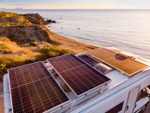 Aerial view. Caravan with solar photovoltaic panels on roof camping on cliff sea shore. 